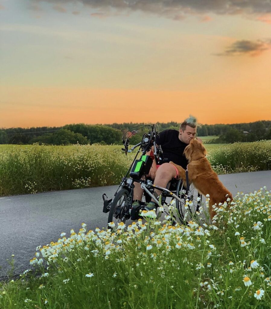 En man sitter på en lipo loma Para cykelfront. Han kysser sin hund. Bakom honom finns en vacker solnedgång.
