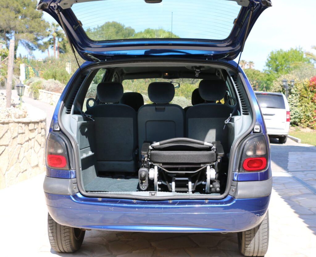 Eloflex P elektrisk rullestol ligger lagt sammen i bagasjerommet på en bil. Bilen er blå og bagasjeromsdøra står oppslått.