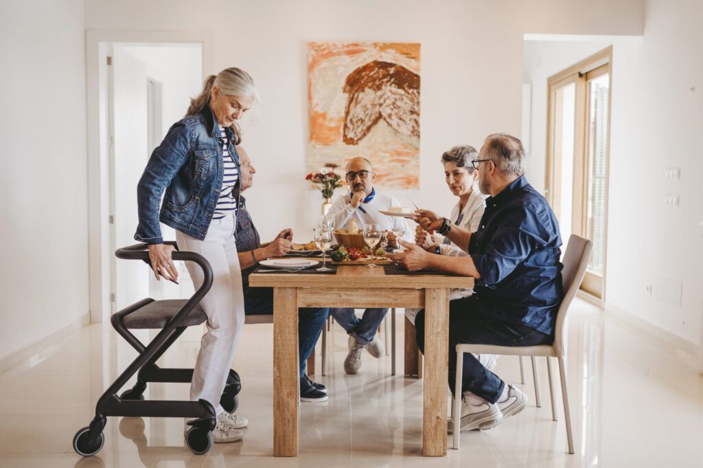 Mennesker sitter rundt bordet og spiser. Dame bruker Saljol Innomhus Rollator